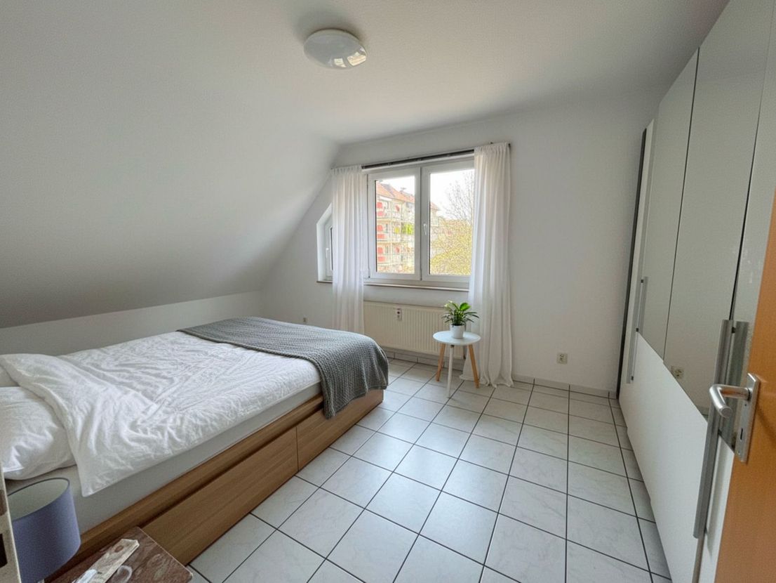 Erstes Schlafzimmer mit Doppelbett, Fenster und weißem Einbauschrank